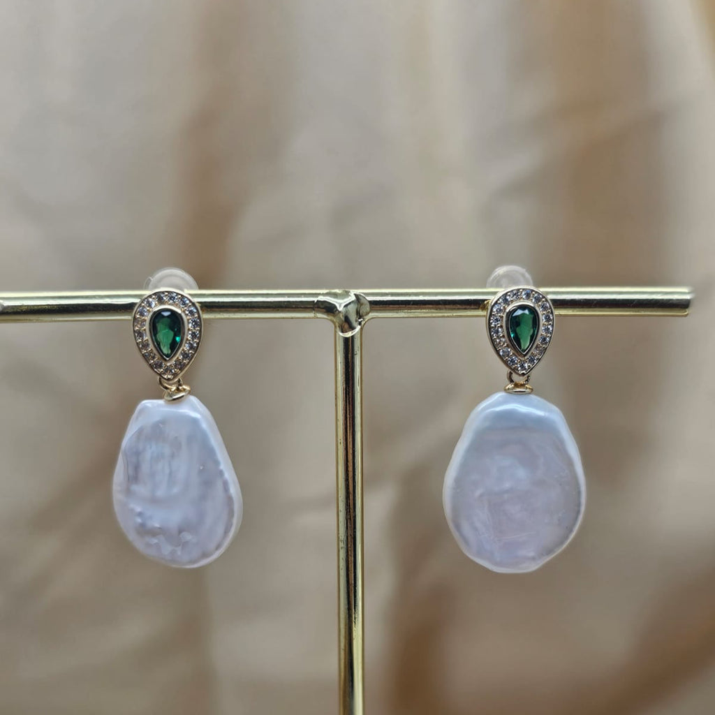 Pearl earrings with green gemstones on a gold stand against a blurred background
