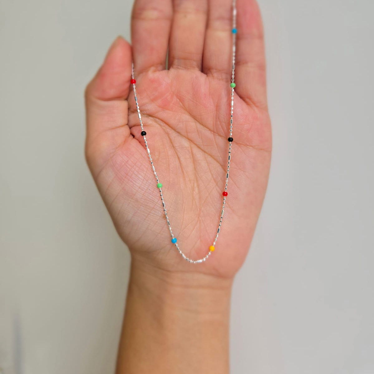 A sterling silver necklace with rainbow-colored dots held in a person's hand.