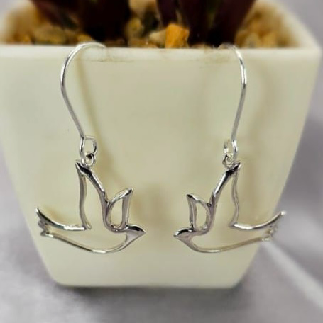 A pair of sterling silver hanging dove earrings displayed in front of a potted plant.