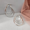 Pair of layered hoop earrings on a light gray surface with a pink fabric background