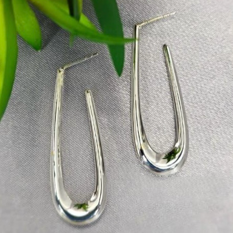 A pair of sterling silver oval tube hoop earrings displayed against a plant backdrop.