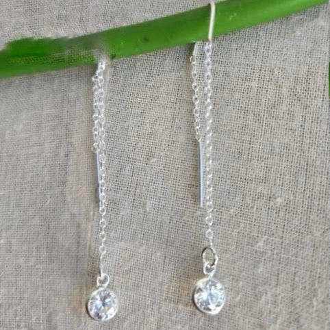 Silver chain earrings with round crystals on a textured fabric background