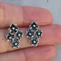 Silver floral earrings held between fingers against a neutral background