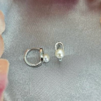 The image displays a pair of sterling silver huggys, each featuring a delicate freshwater pearl. The huggys are designed with a simple yet elegant hoop structure, and the pearls are set within the hoops, adding a touch of natural beauty and sophistication.