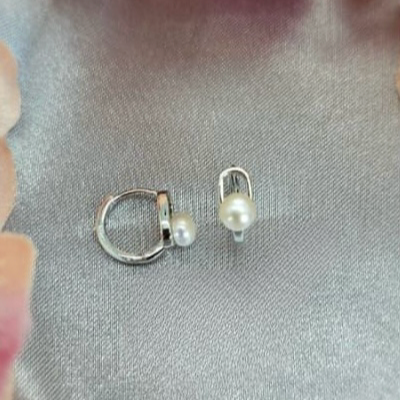 The image displays a pair of sterling silver huggys, each featuring a delicate freshwater pearl. The huggys are designed with a simple yet elegant hoop structure, and the pearls are set within the hoops, adding a touch of natural beauty and sophistication.