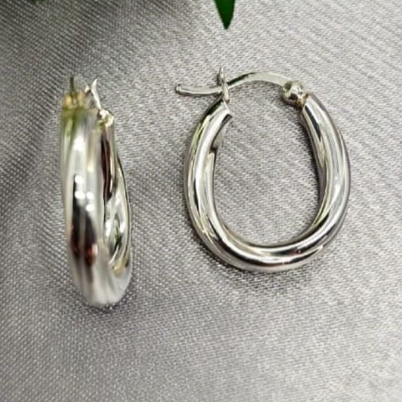 A pair of sterling silver oval hoop earrings displayed on a table with a blurred green leaf in the background.