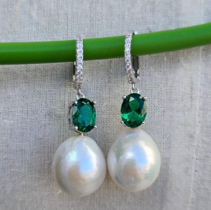 Pearl earrings with green gemstones on a gray background