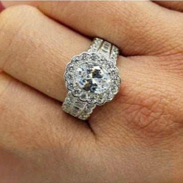 An oval-shaped sterling silver ring encrusted with multiple cubic zirconia stones, displayed on a person's finger.