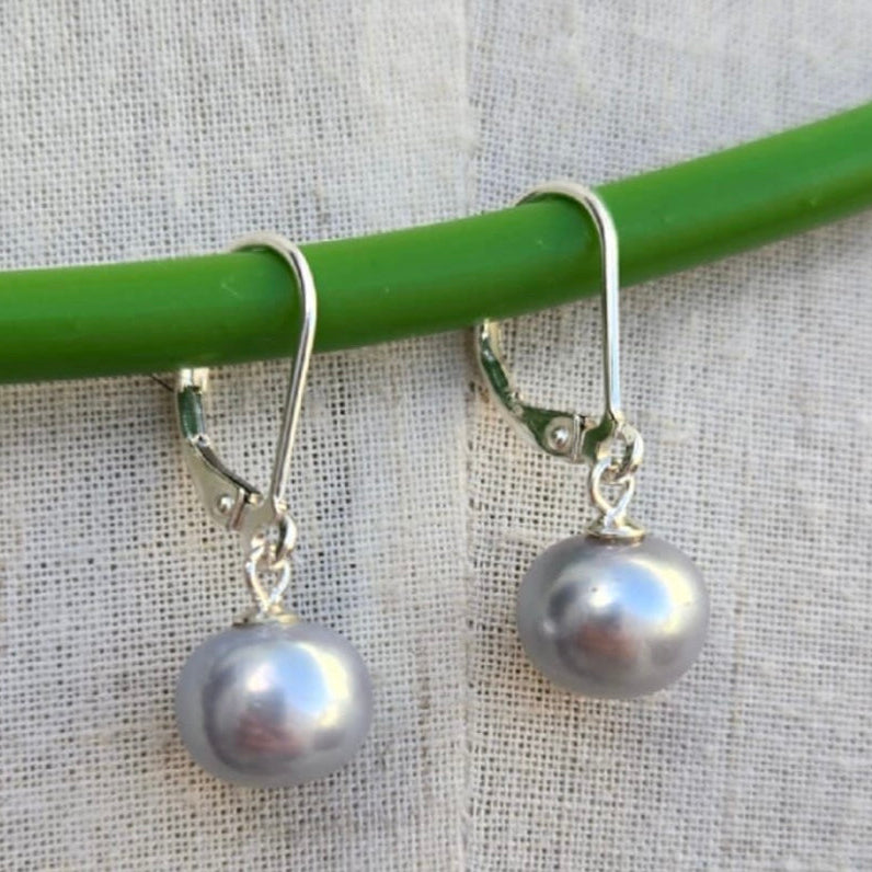 Pearl earrings hanging on a green rod with a light fabric background