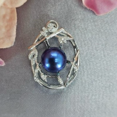 A sterling silver pendant featuring a blue pearl in the center, with cubic zirconia accents around the edge, displayed against a soft grey background with flower petals scattered around.