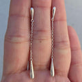 Silver chain earrings held between two fingers against a neutral background