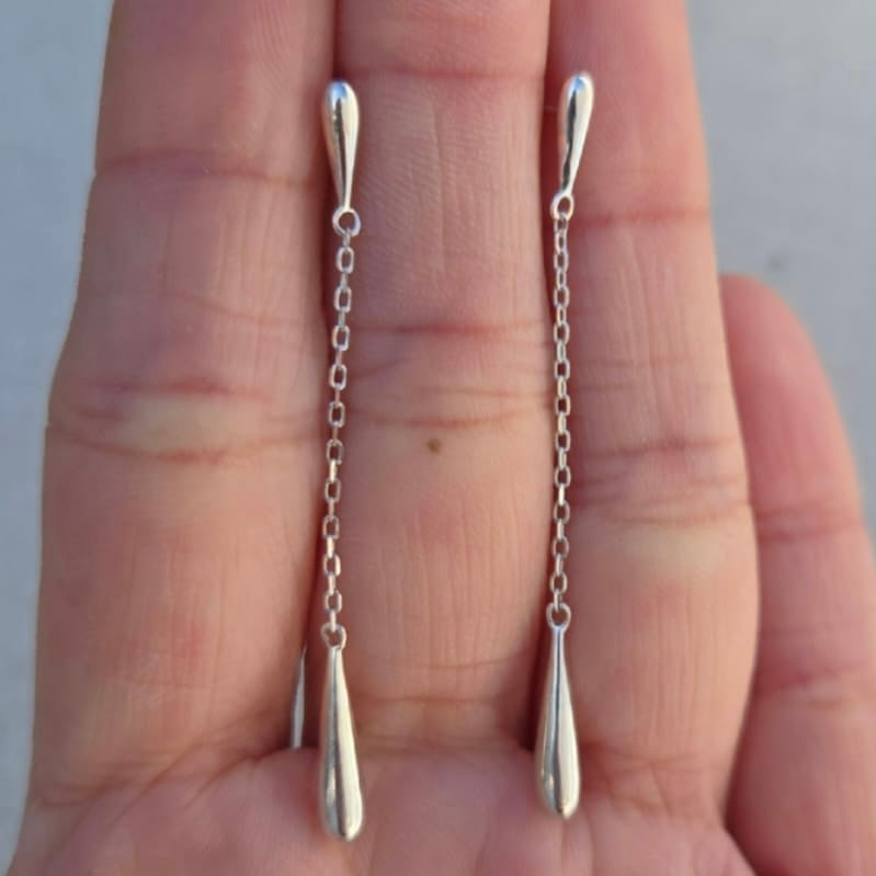 Silver chain earrings held between two fingers against a neutral background