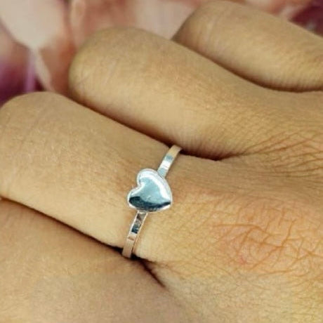 A person's hand displaying a sterling silver puffy heart ring on their finger.