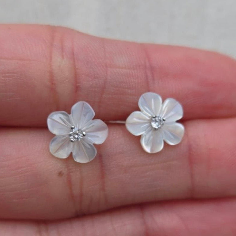 Flower-shaped earrings held between fingers against a neutral background