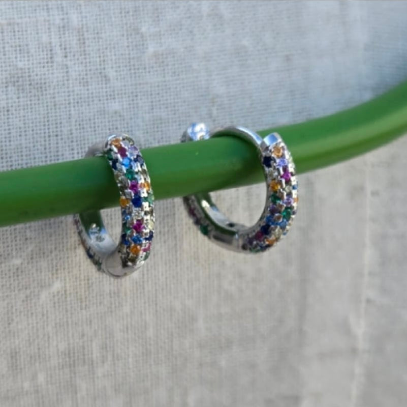 Silver hoop earrings with colorful stones on a green stick against a neutral background