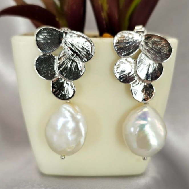 A pair of silver flower earrings with pearl accents displayed in a white vase with green leaves.