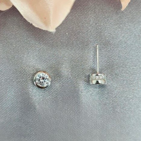 Silver earrings with clear gemstones on a gray surface with pink flowers in the background