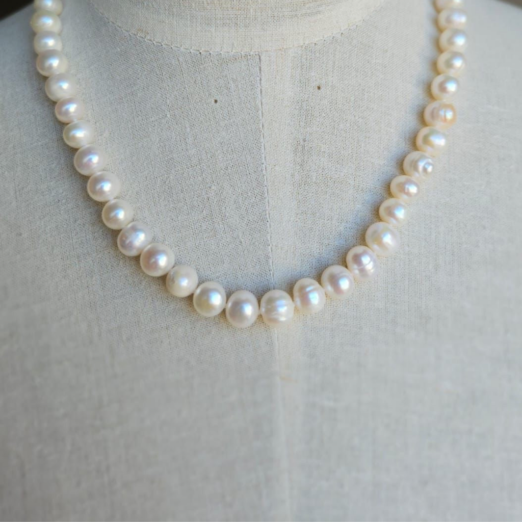 A white pearl necklace displayed on a mannequin torso.