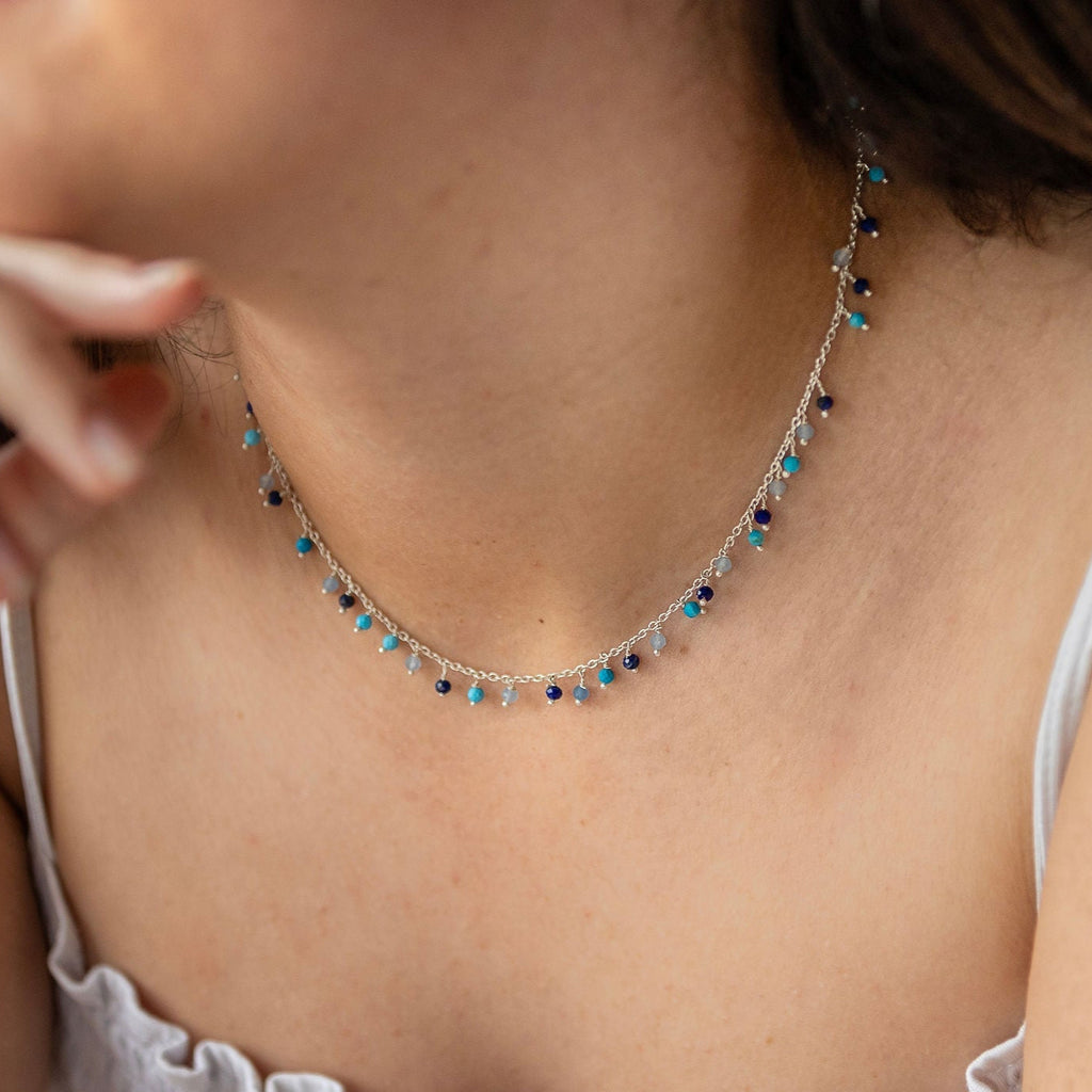 A person wearing a sterling silver necklace with turquoise, lapis, and calcy semi-precious stones.