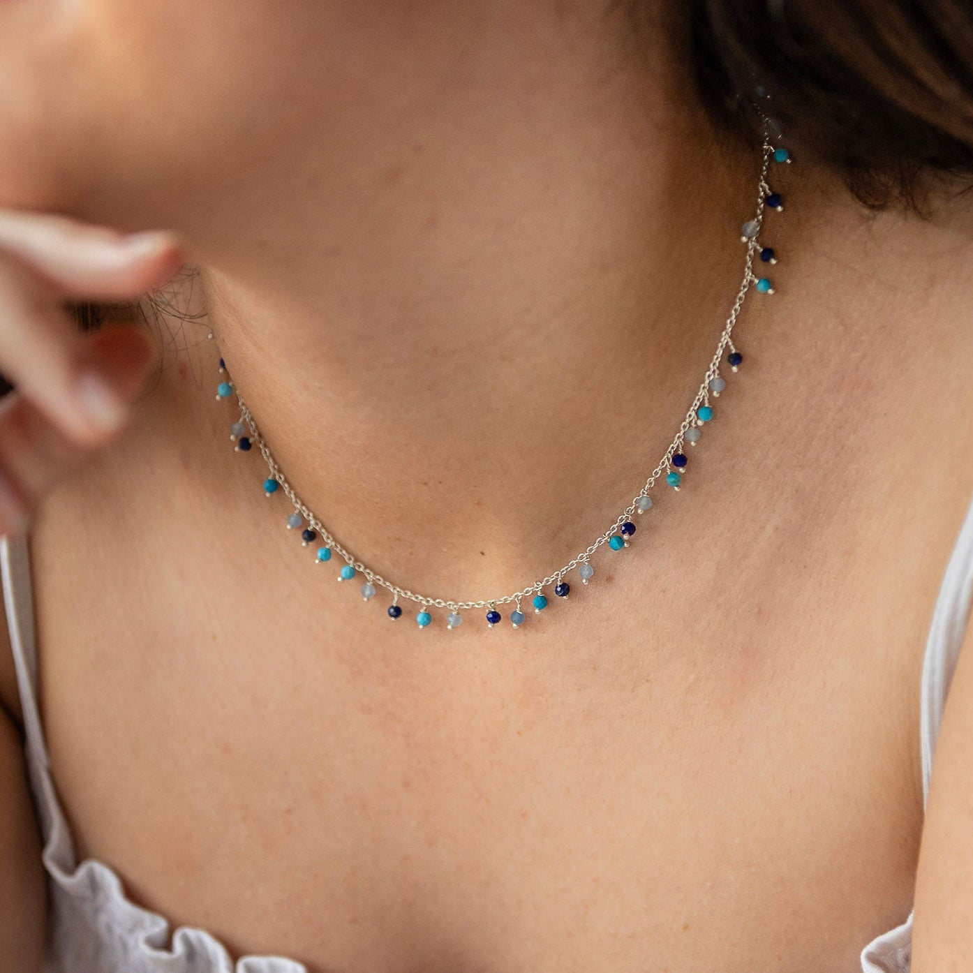 A person wearing a sterling silver necklace with turquoise, lapis, and calcy semi-precious stones.