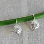 Silver earrings hanging from a green rod against a textured gray background