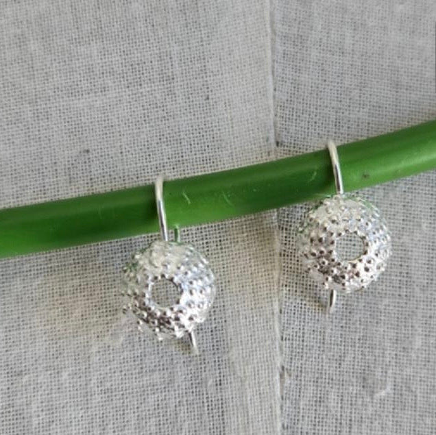 Silver earrings hanging from a green rod against a textured gray background