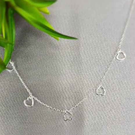 A sterling silver necklace with multiple tiny open heart shapes attached to the chain, displayed on a grey background with a green plant leaf for scale.