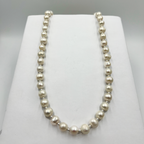 A white pearl necklace with sterling silver small ball links displayed on a white stand.