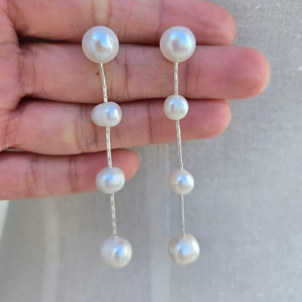 Pearl earrings held between fingers against a neutral background
