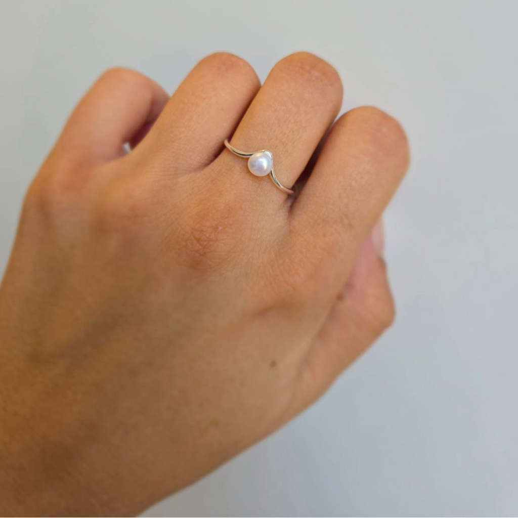 A sterling silver adjustable wishbone ring with a freshwater pearl center displayed on a person's hand.