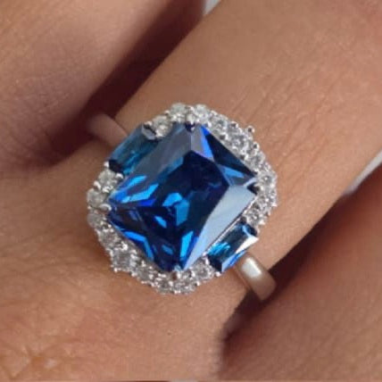 Ring with a blue gemstone and silver halo on a finger