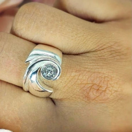 A sterling silver wave ring with a central cubic zirconia gemstone, displayed on a person's finger.
