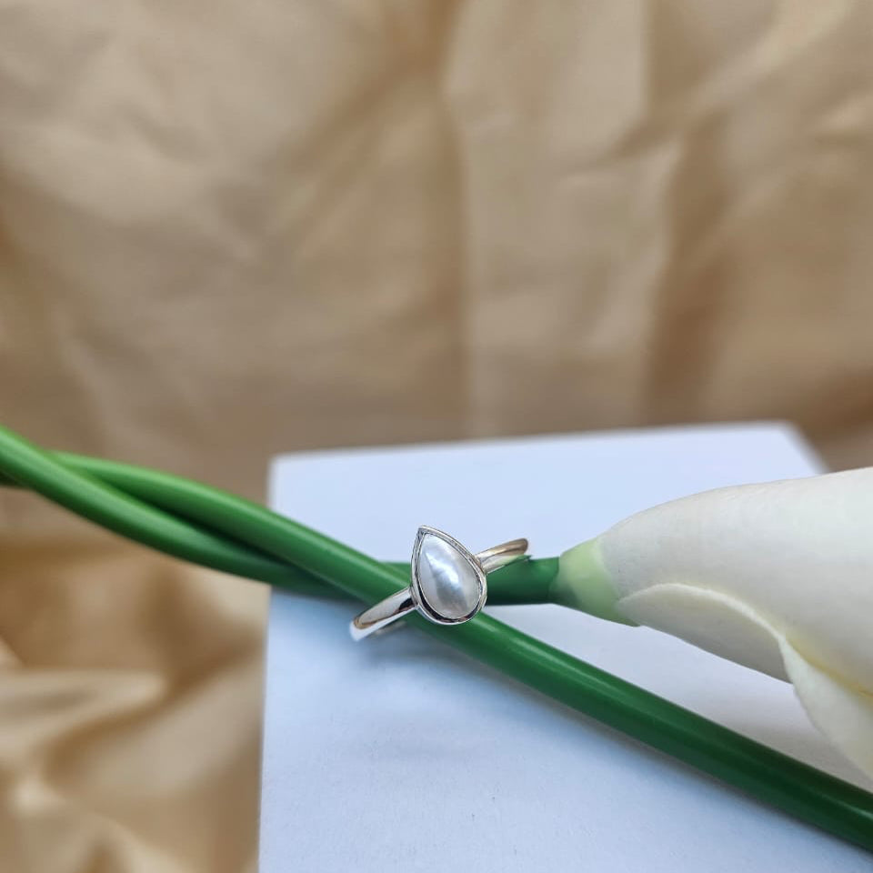 Silver ring with a pearl on a white card with green stem and beige background