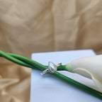 Silver ring with a pearl on a white card with green stem and beige background
