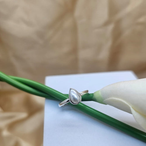 Silver ring with a pearl on a white card with green stem and beige background