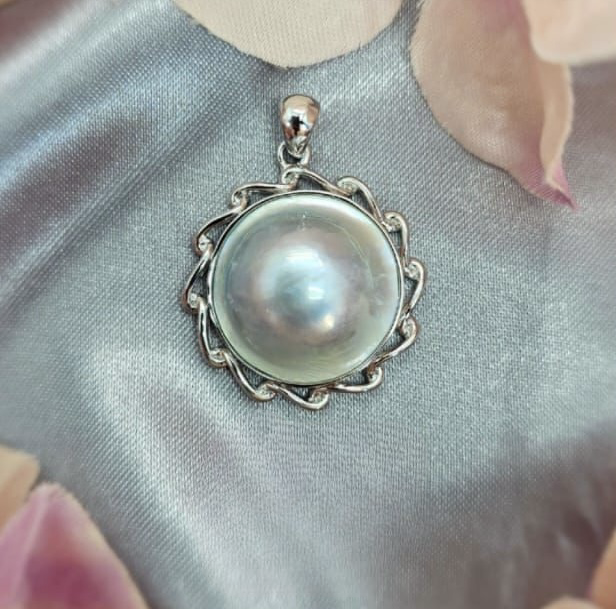 A Blue/Grey Blister Mabe Pearl pendant set in Sterling silver, displayed against a fabric background.