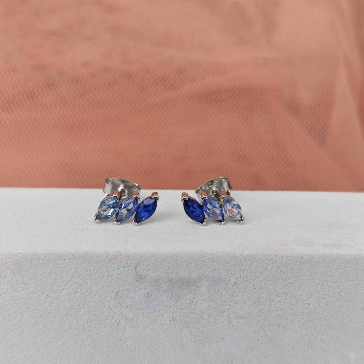 Pair of blue gemstone earrings on a white surface with a pink fabric background