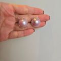 A pair of pink Mabe pearl stud earrings set in sterling silver, held in a person's hand.