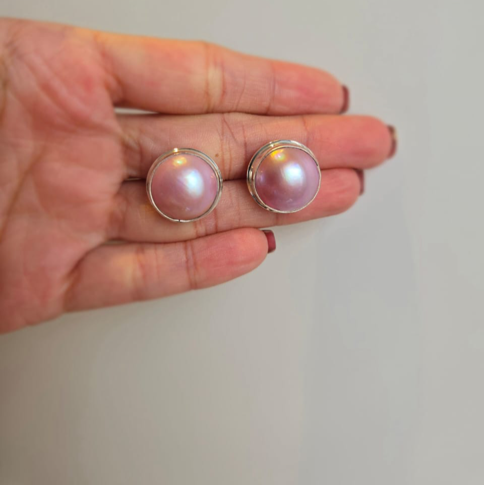 A pair of pink Mabe pearl stud earrings set in sterling silver, held in a person's hand.