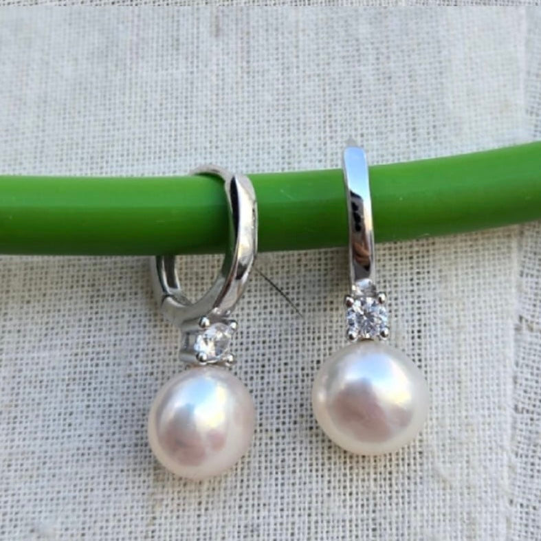 Pearl earrings with silver hooks on a green stick against a textured white background