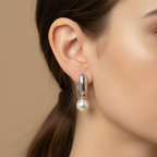 A pair of sterling silver drop earrings with pearls on end, displayed in a white container with a green plant in the background.