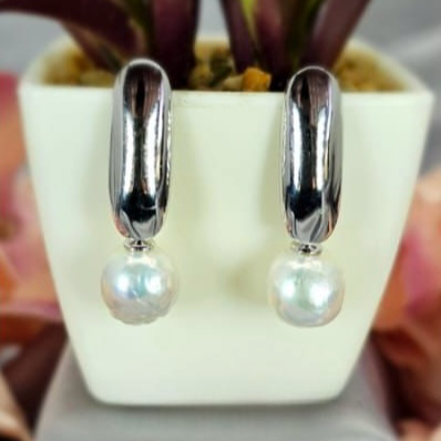 A pair of sterling silver drop earrings with pearls on end, displayed in a white container with a green plant in the background.