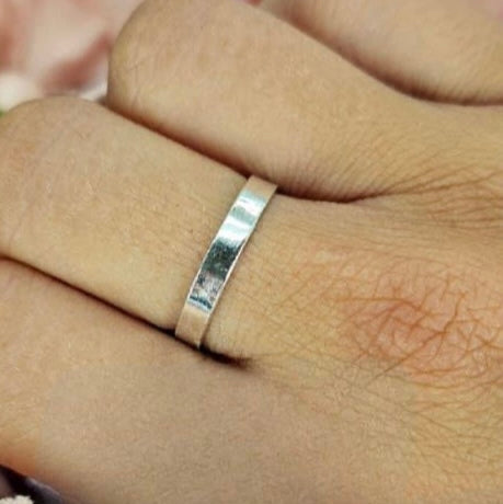 A sterling silver band ring worn on a person's finger, showing a plain and sleek design.