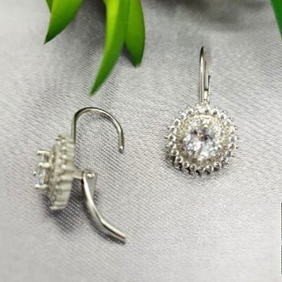 Silver earrings with clear gemstones on a gray surface with green leaves in the background
