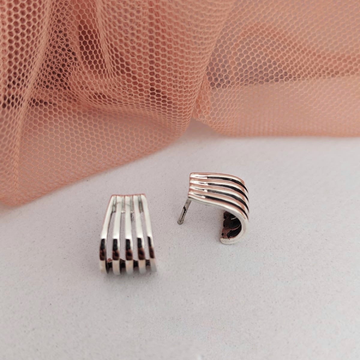 Pair of silver earrings on a light gray surface with a pink fabric background