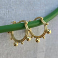 Gold hoop earrings with spherical accents on a green stick against a light fabric background