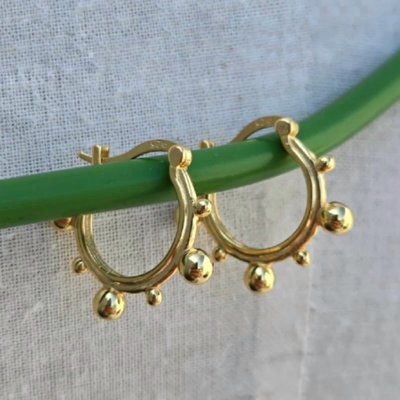 Gold hoop earrings with spherical accents on a green stick against a light fabric background
