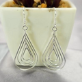 A pair of silver teardrop-shaped drop earrings displayed in front of a white vase with a green plant.
