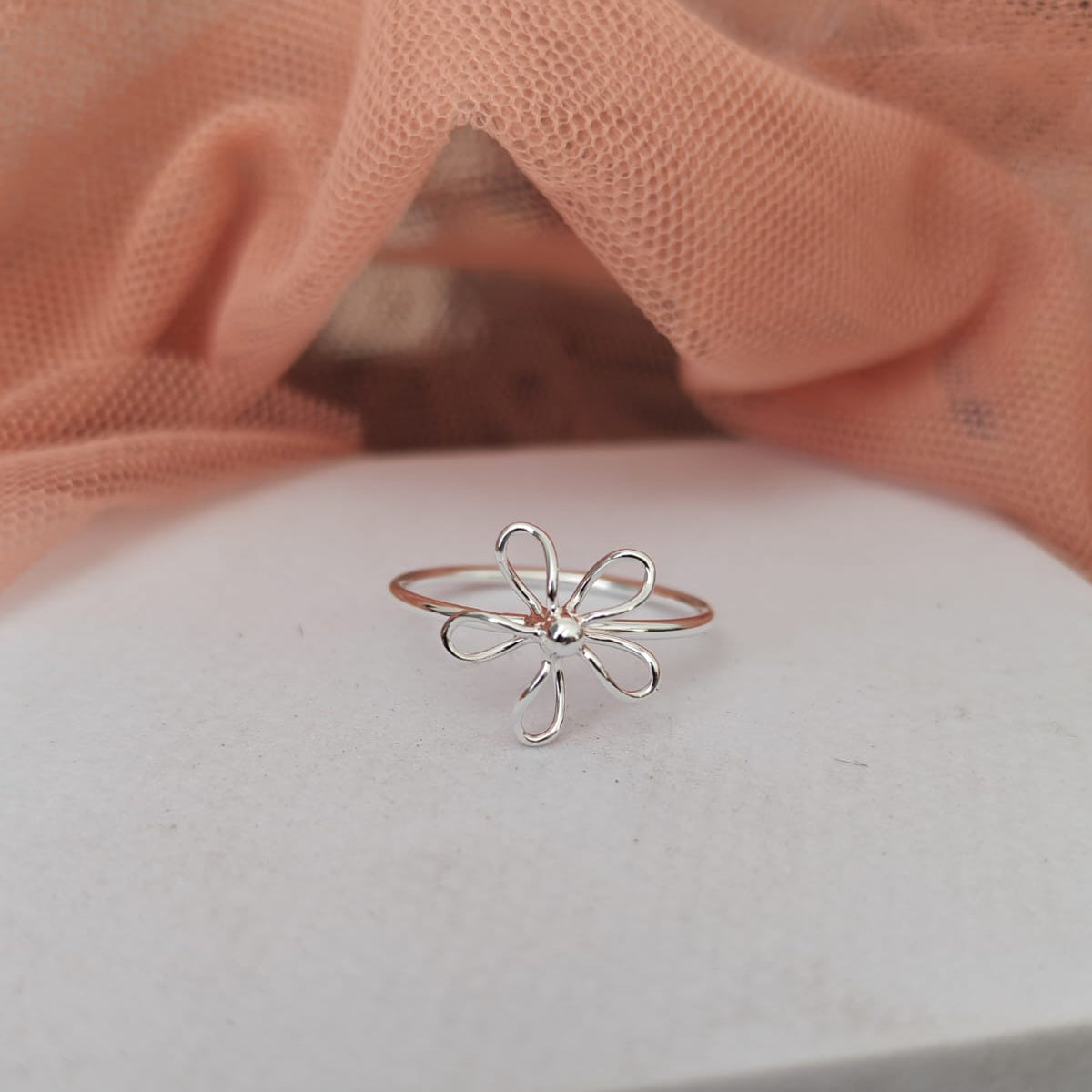 Silver flower-shaped ring on a white surface with a pink fabric background