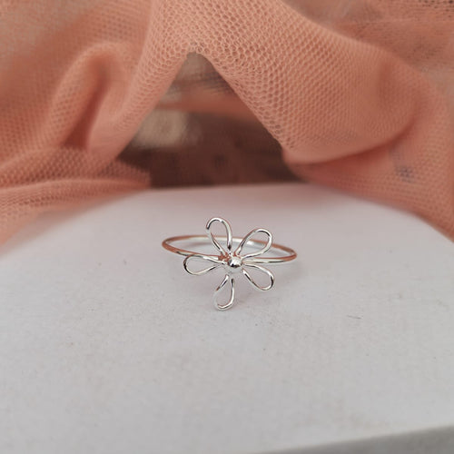 Silver flower-shaped ring on a white surface with a pink fabric background